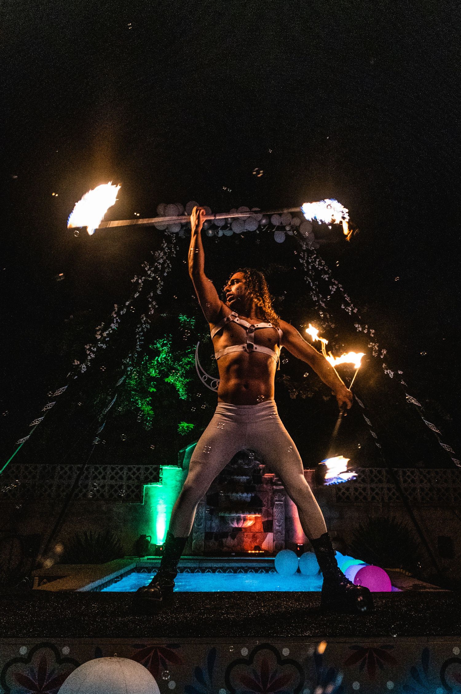 Fire performers entertain at a nighttime pool party with colorful lighting and dramatic flame effects.