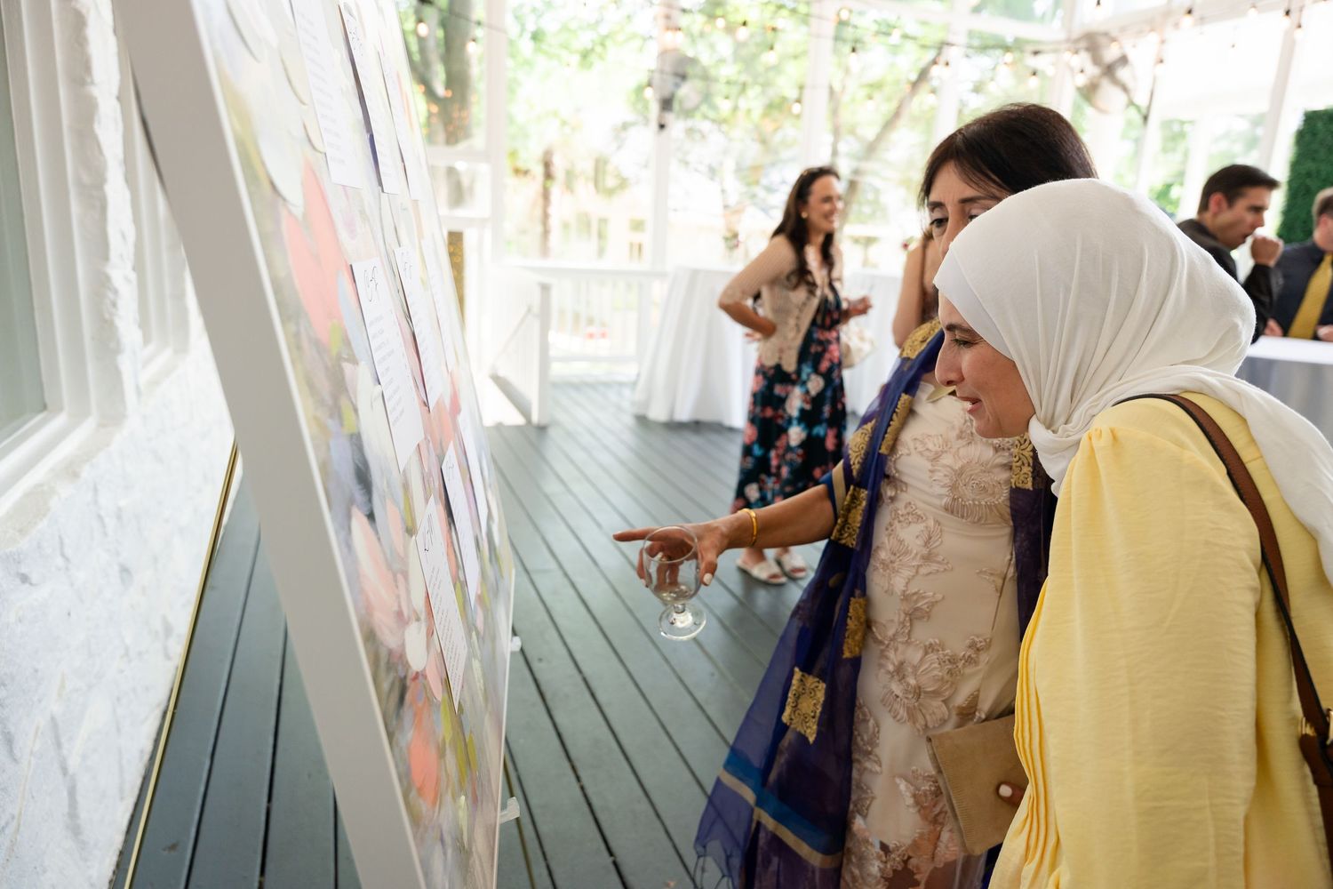 Two women examining colorful artwork display at an outdoor gallery event on a wooden deck.