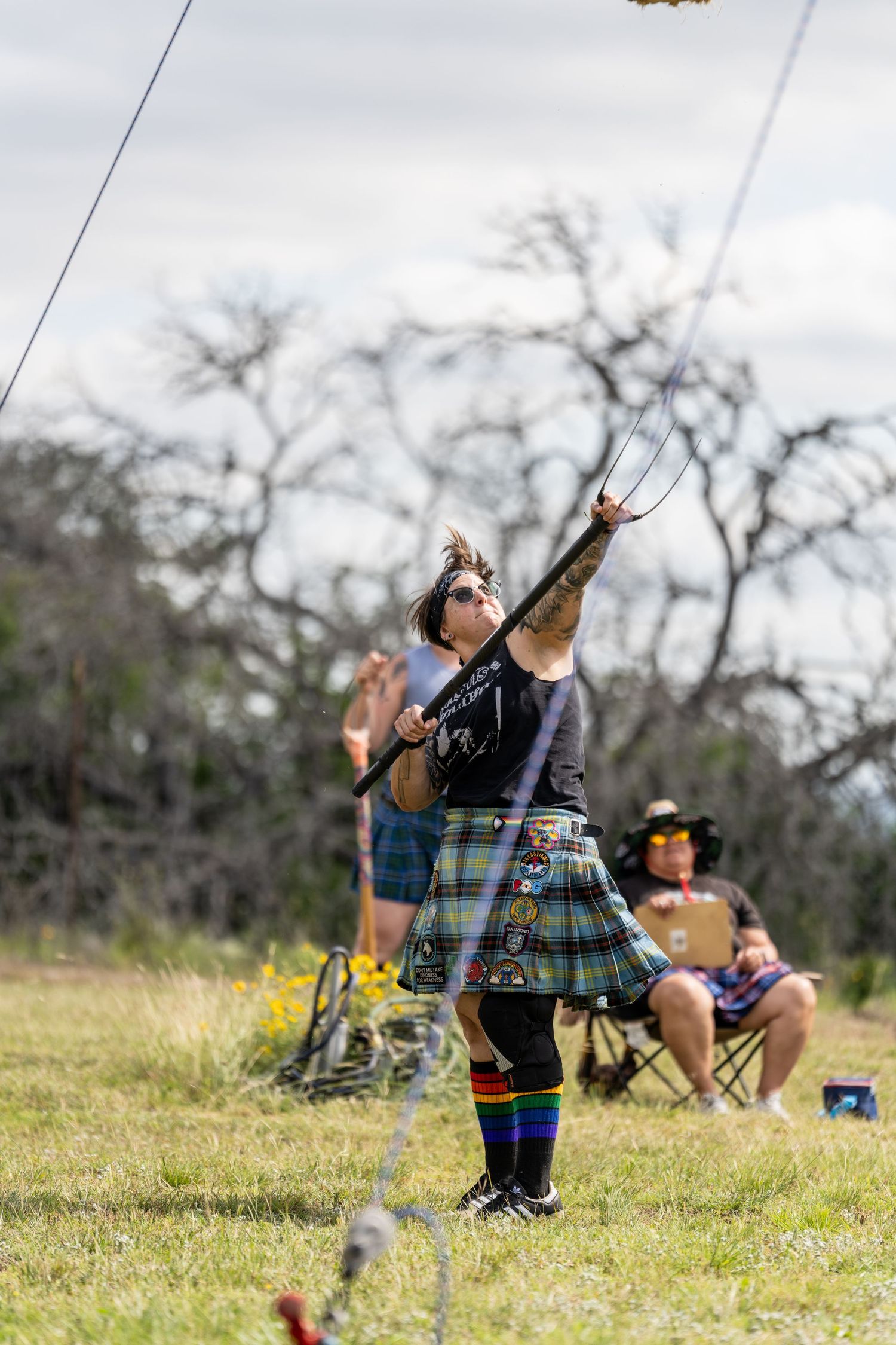 Person in tartan kilt throwing a caber at a Scottish Highland Games competition outdoors.