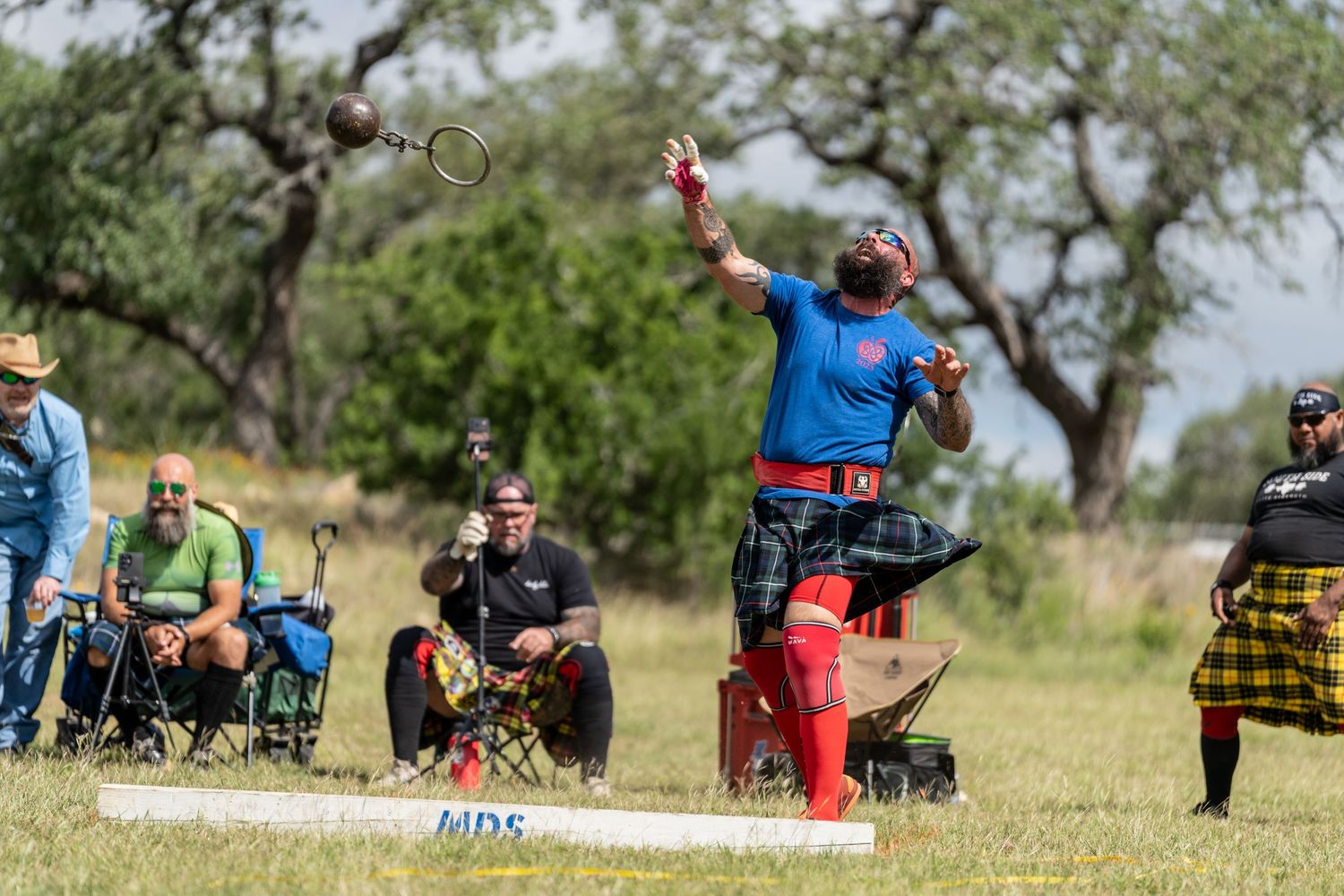 Athlete competes in Highland Games hammer throw event outdoors, with spectators watching in traditional Scottish attire.