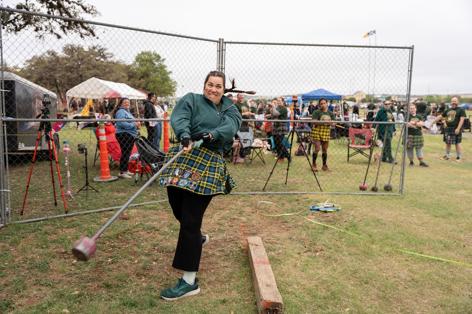 Woman in tartan kilt competing in Highland Games hammer throw event at outdoor Scottish festival.