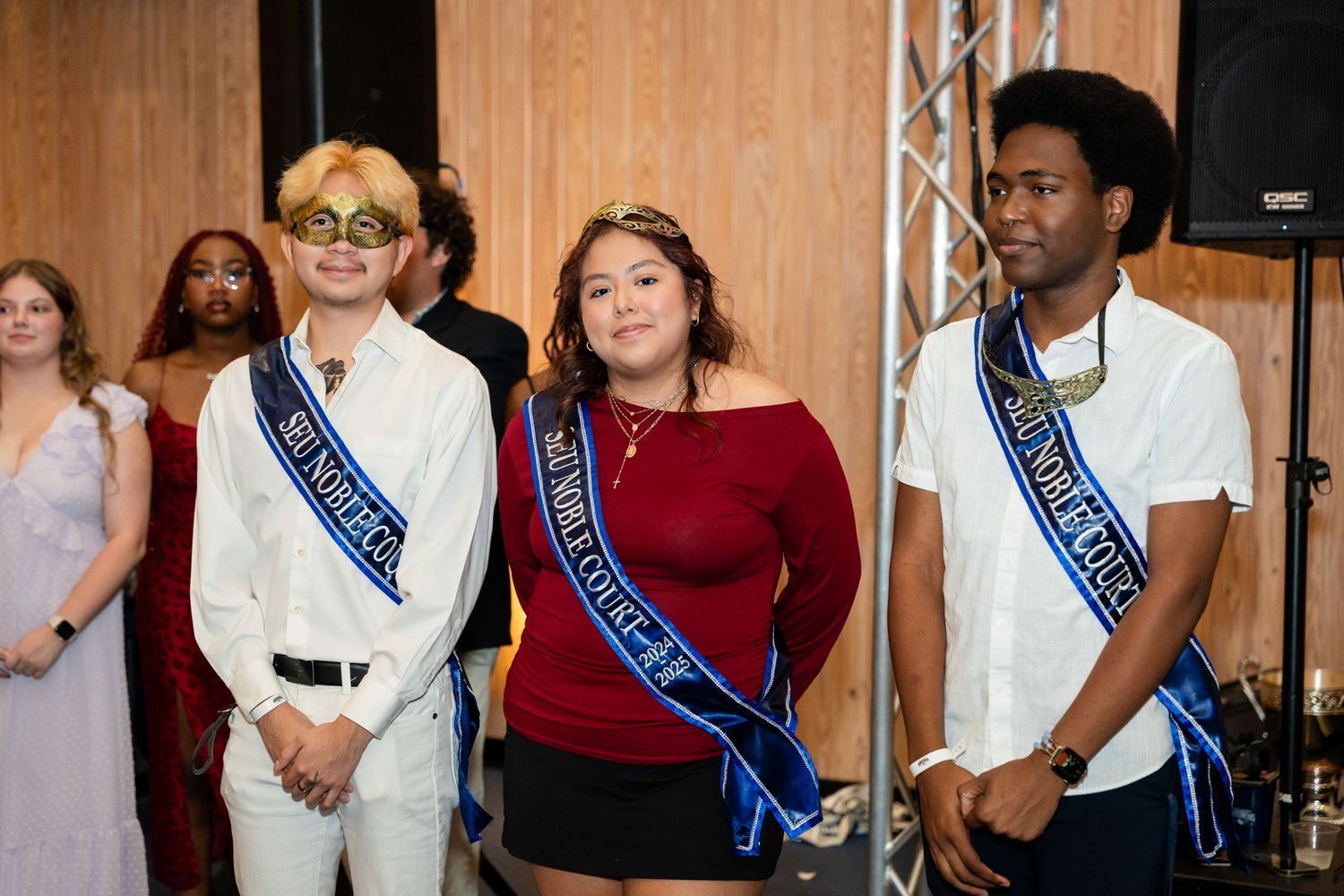 Several students wearing blue sashes stand together at a formal event.
