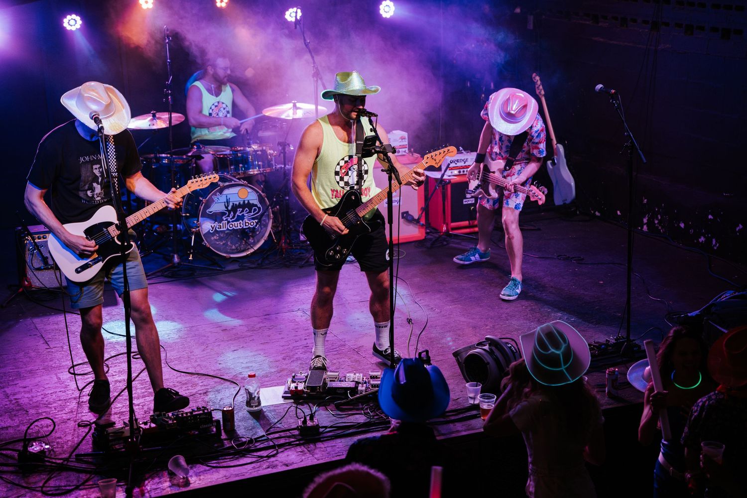 Band performing on stage with purple lighting and smoke effects at a concert venue.