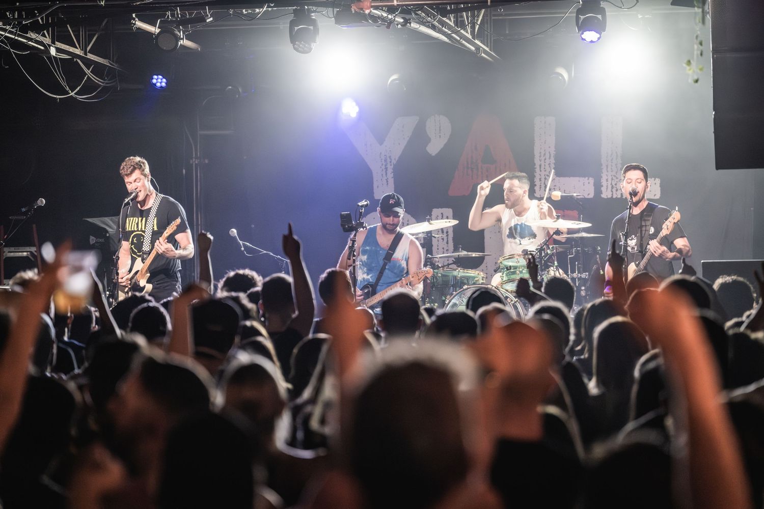 Rock band performing on stage with crowd raising hands at energetic concert.