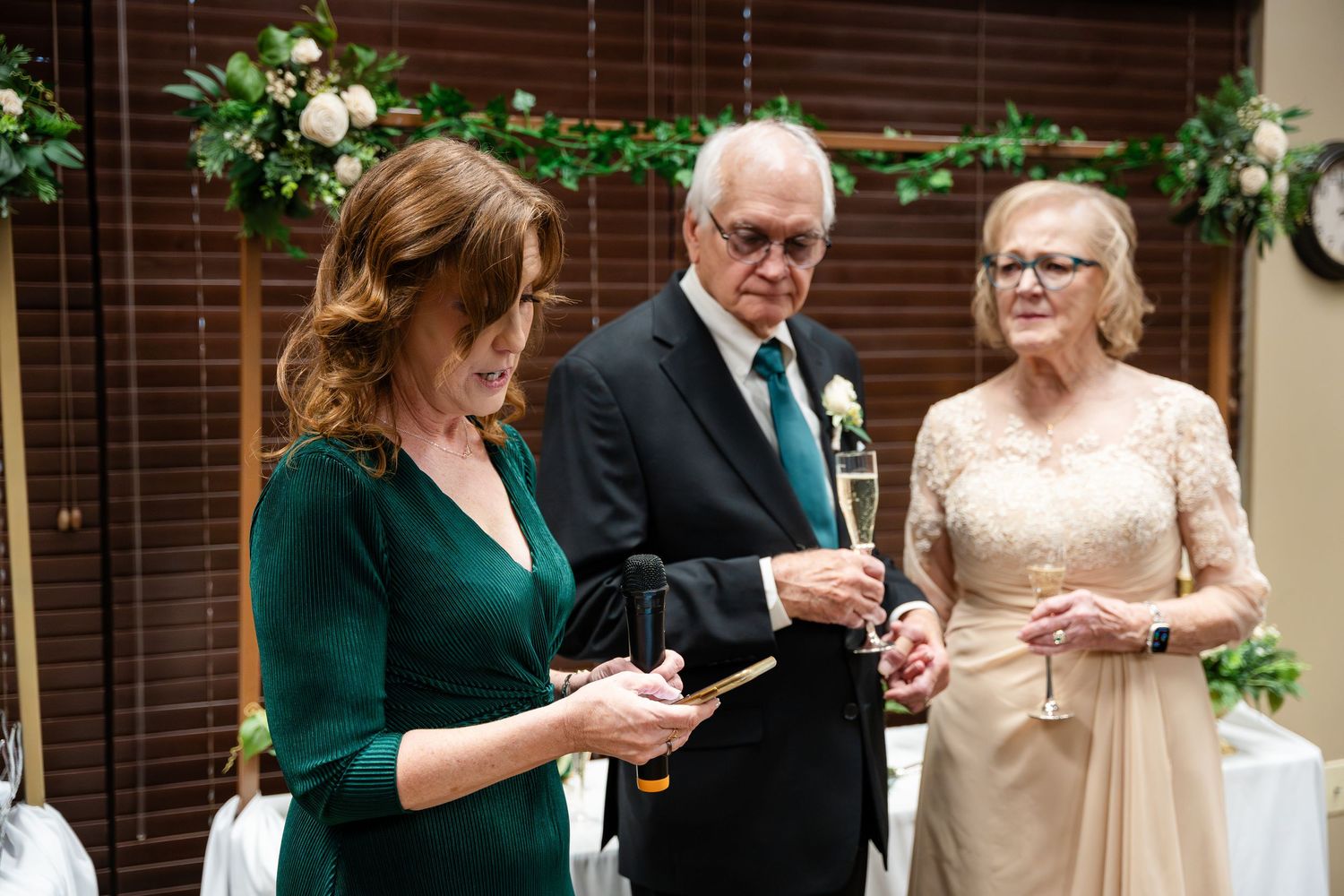 Three people sharing a moment in formal attire at an elegant event with a green vine-decorated backdrop.