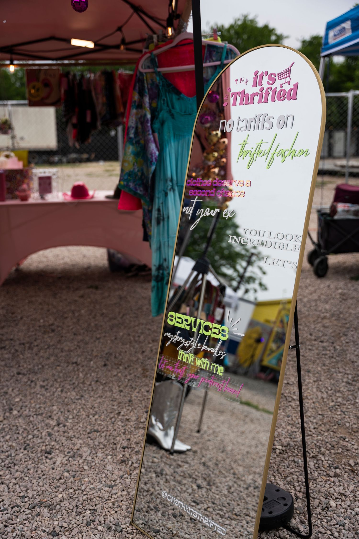 A series of five tent signs with handwritten text stand in a gravel area at an outdoor event or market.