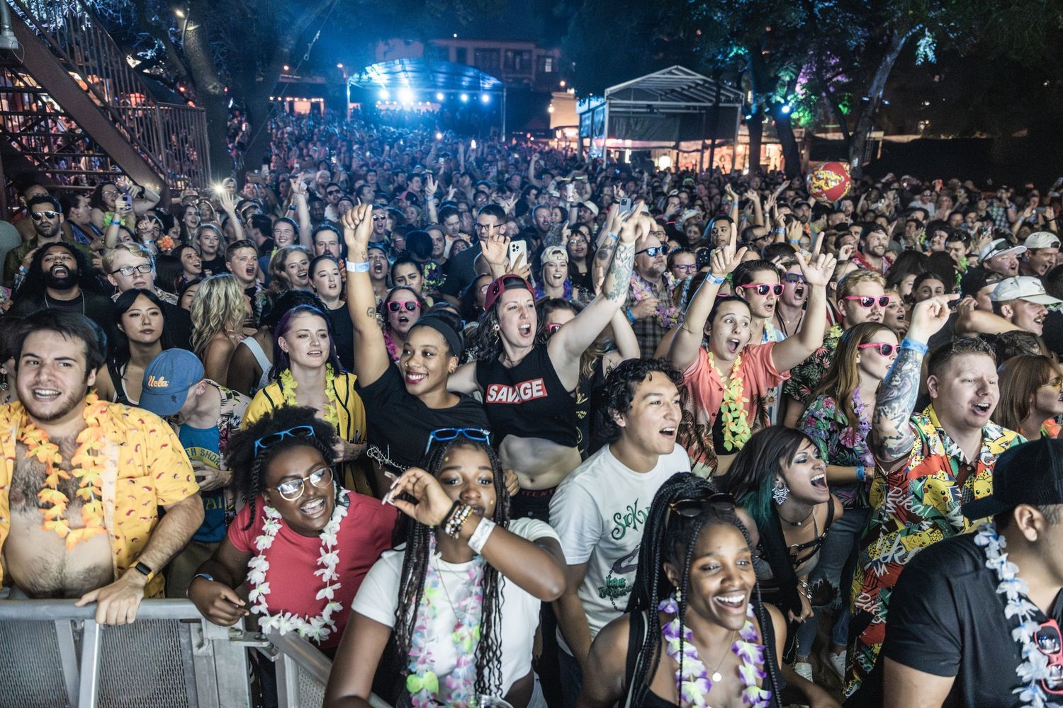 Enthusiastic festival crowd wearing colorful leis and summer attire enjoying outdoor concert.