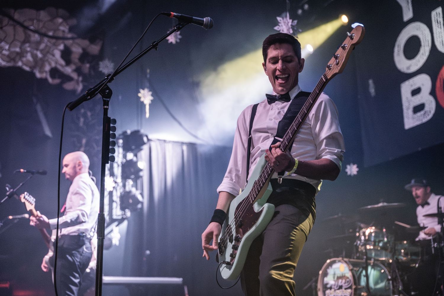 Musicians perform on stage with dramatic concert lighting and snowflake decorations.