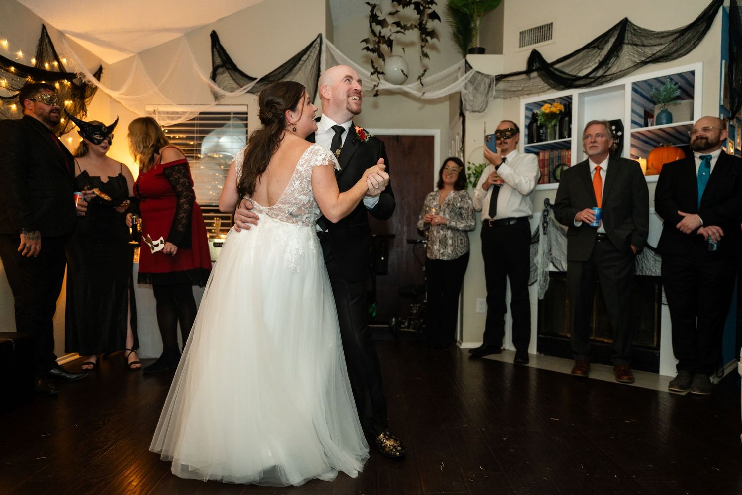 Wedding couple shares first dance surrounded by guests in decorated indoor venue.