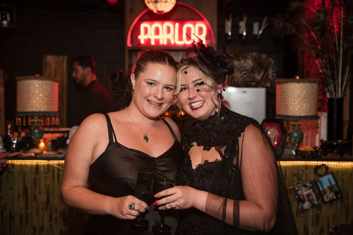 Two friends smiling and enjoying a party under a red neon Parlor sign.