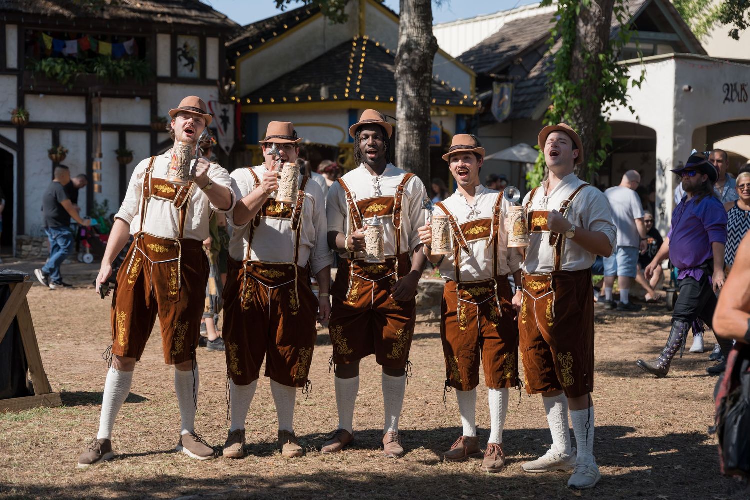 A group in traditional Bavarian lederhosen poses together at an outdoor festival.
