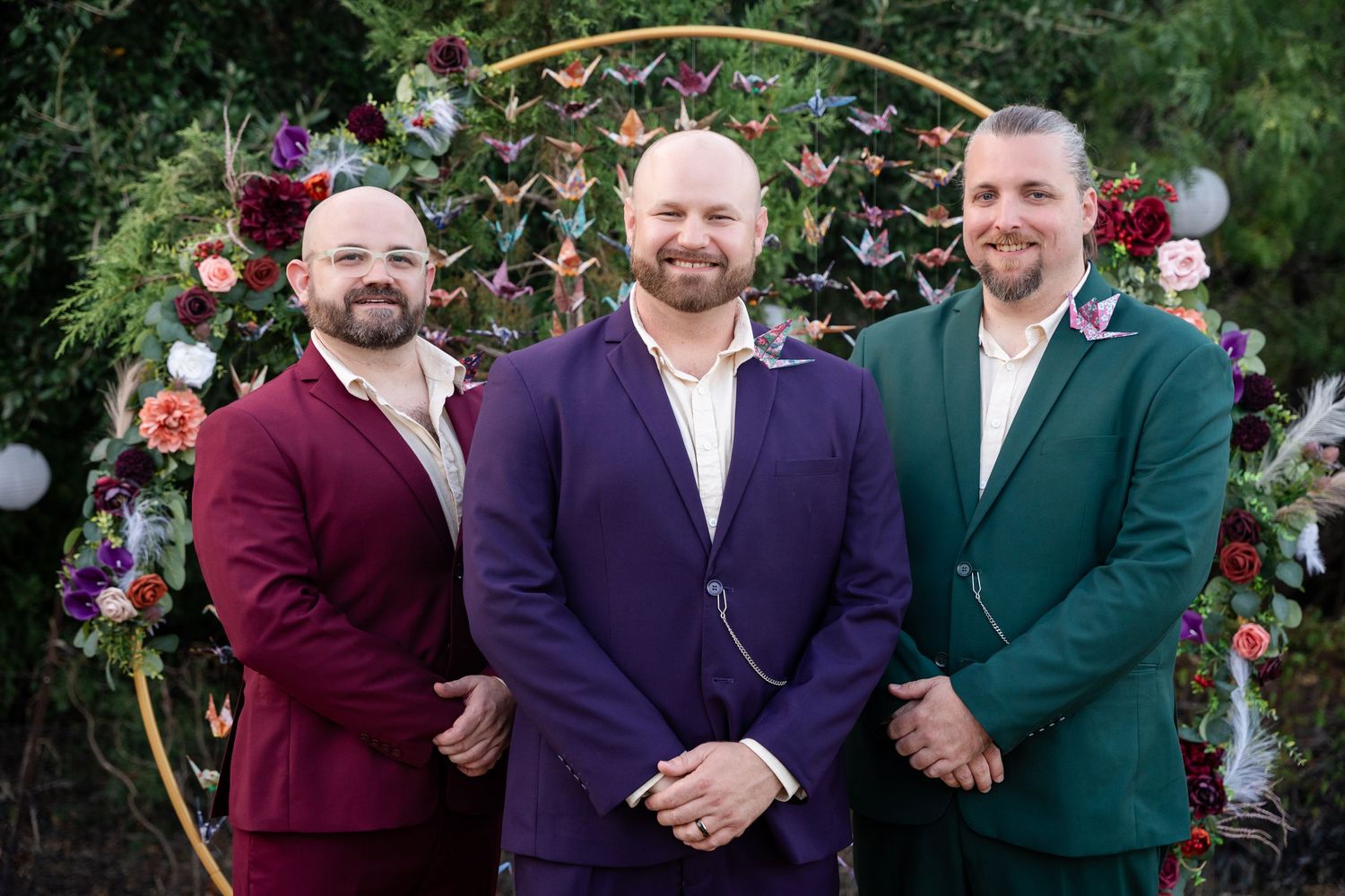Three people in formal attire pose in front of a decorative golden arch with paper butterflies.
