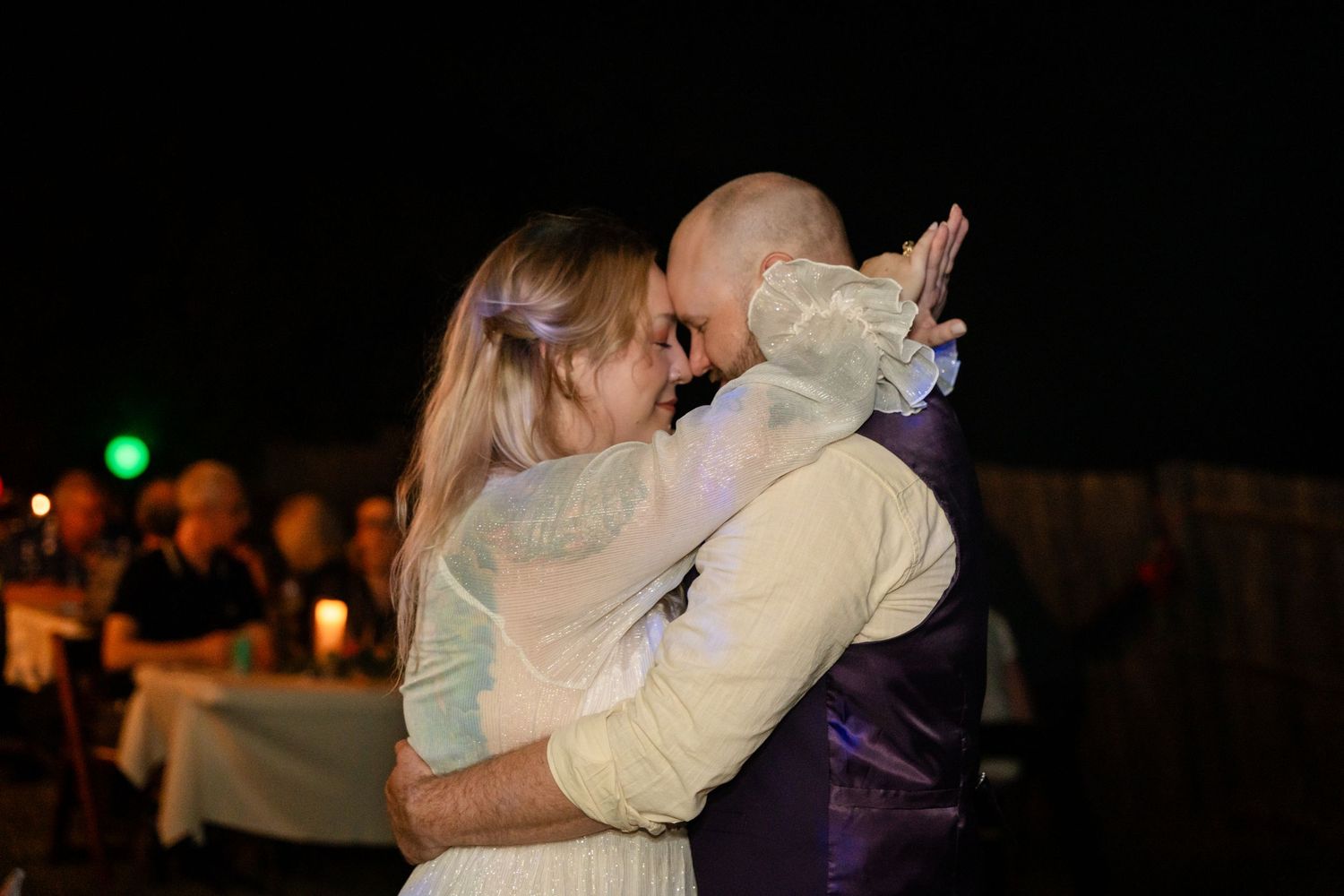 Couple embraces while dancing at nighttime wedding celebration.