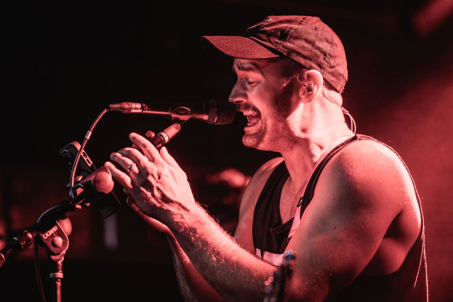 Passionate performer singing into microphone on stage with dramatic red lighting.
