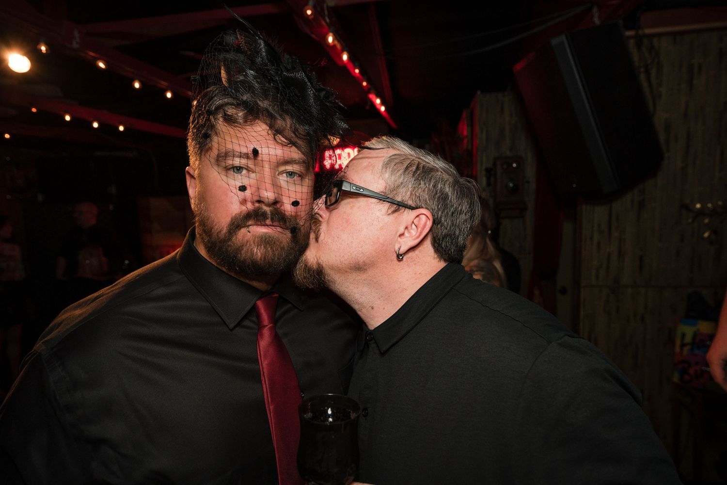 Two people sharing an intimate moment at a dimly lit venue with red lighting in the background.