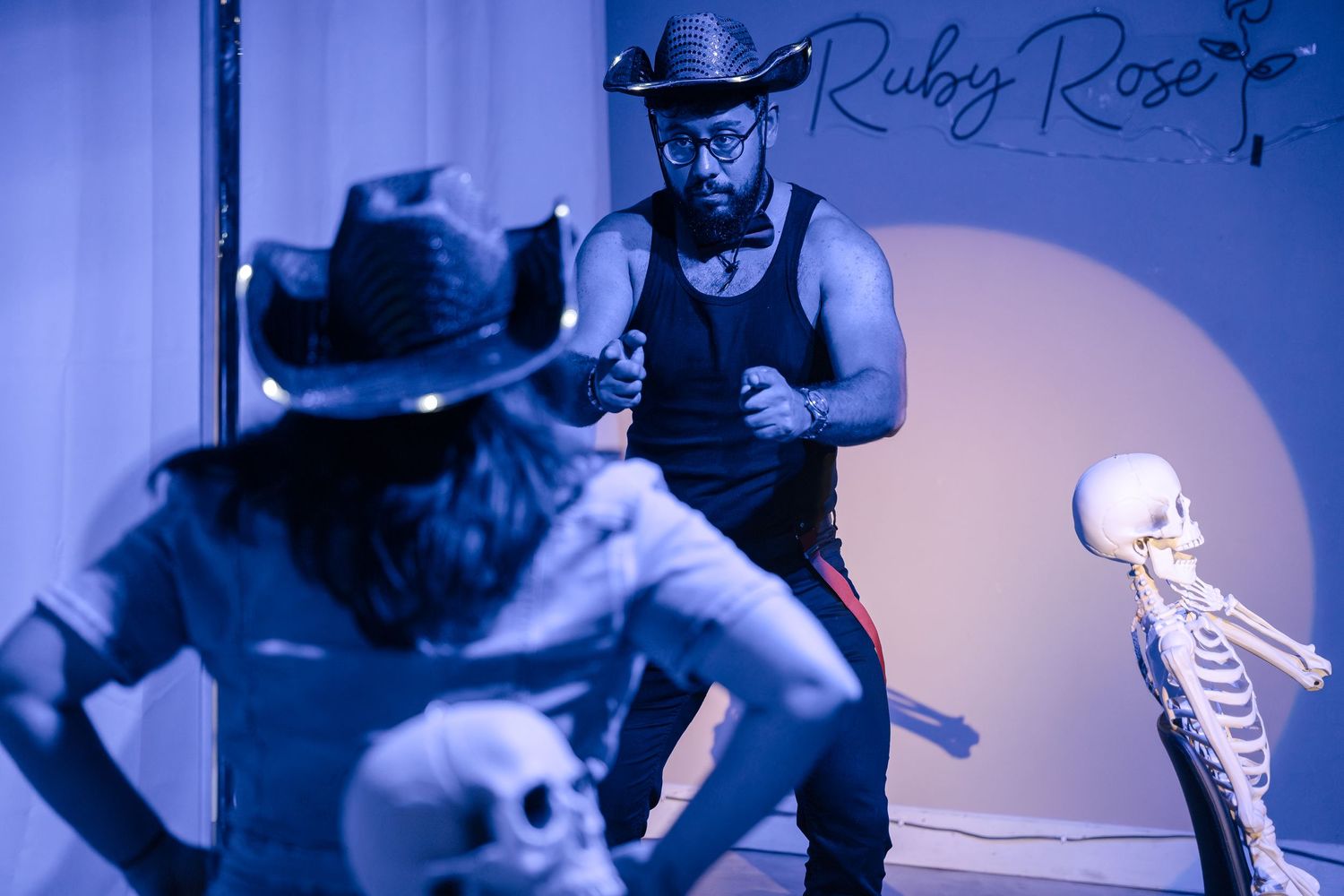 Western-themed performance scene with cowboy hats and skeleton props in blue lighting.