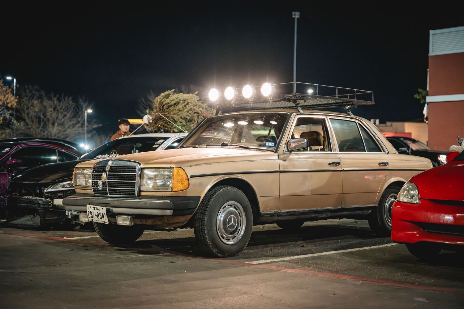 Classic beige Mercedes-Benz sedan with roof-mounted lights at a nighttime car meet.