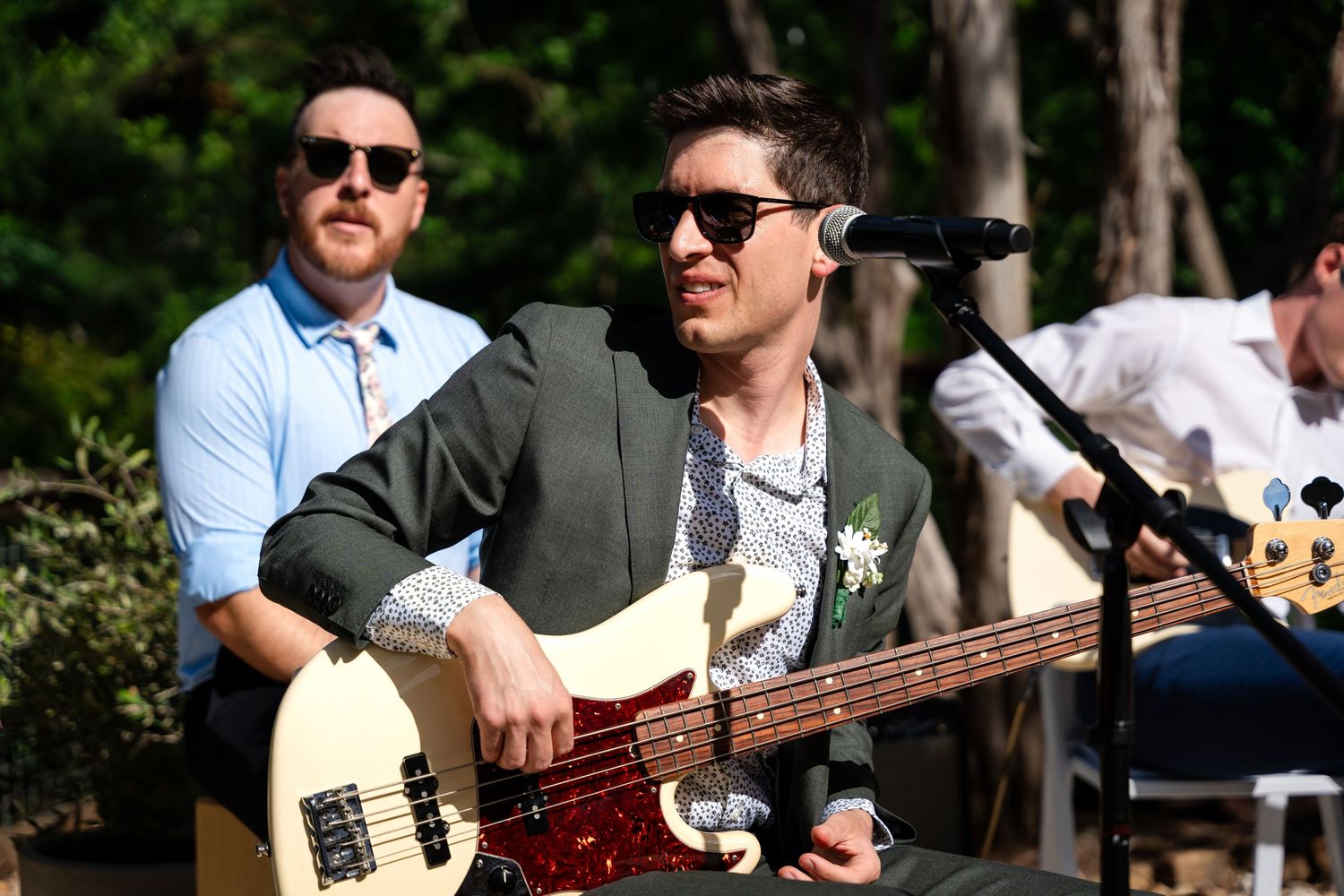 Musicians performing at an outdoor event with bass guitar and sunglasses.