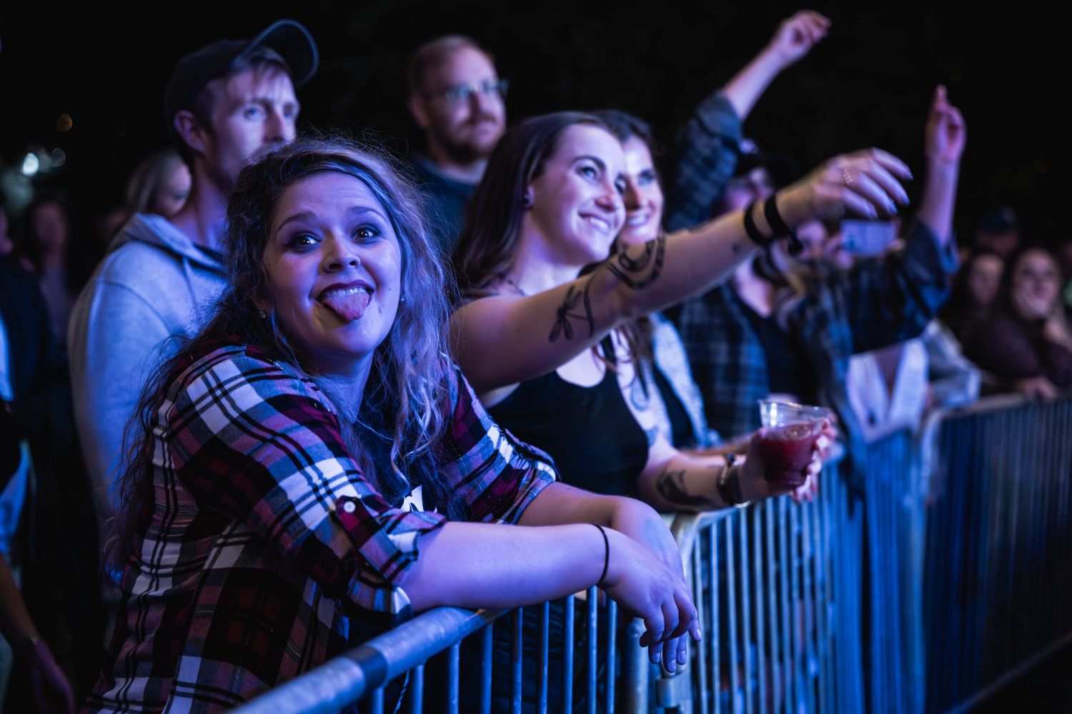 Concert attendees cheering behind security barrier at a live music show.
