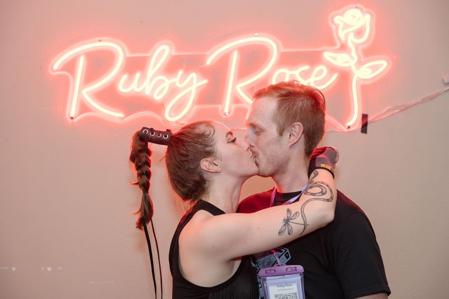 A couple shares an intimate moment under a glowing neon 'Ruby Rose' sign.