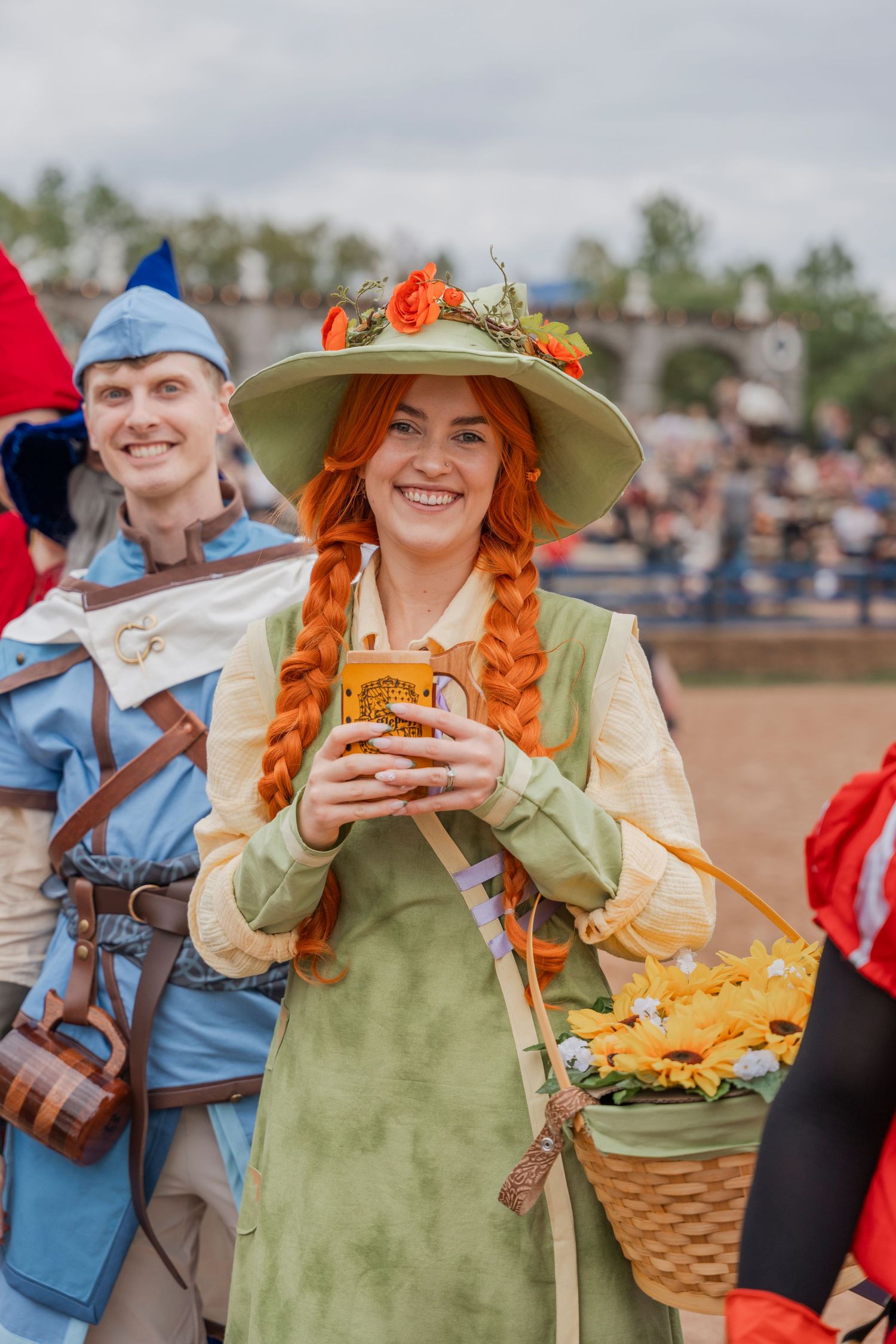 Woman in medieval dress with braided hair and flower hat holding drink at renaissance faire.