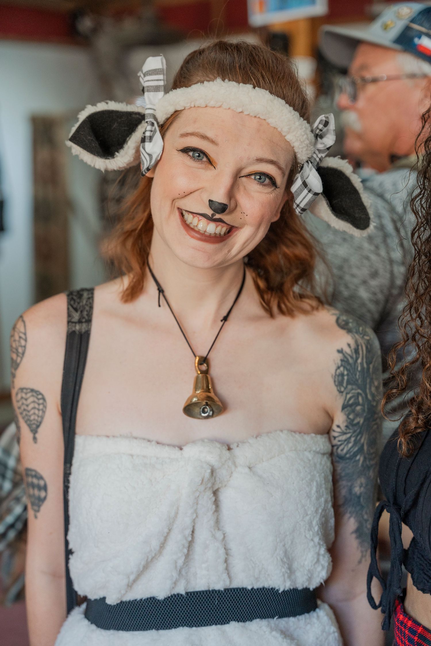 Festival attendee in white sheep costume with face paint and bell necklace.