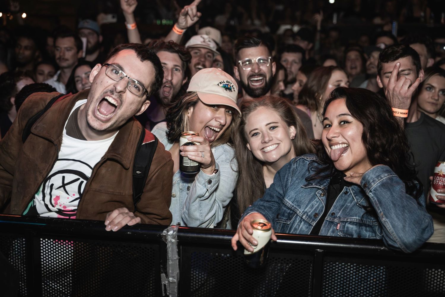 Concert attendees smiling and enjoying a live performance behind a venue barrier.