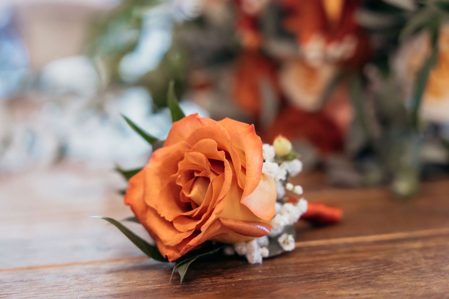 Single orange rose boutonniere with baby's breath on wooden surface.