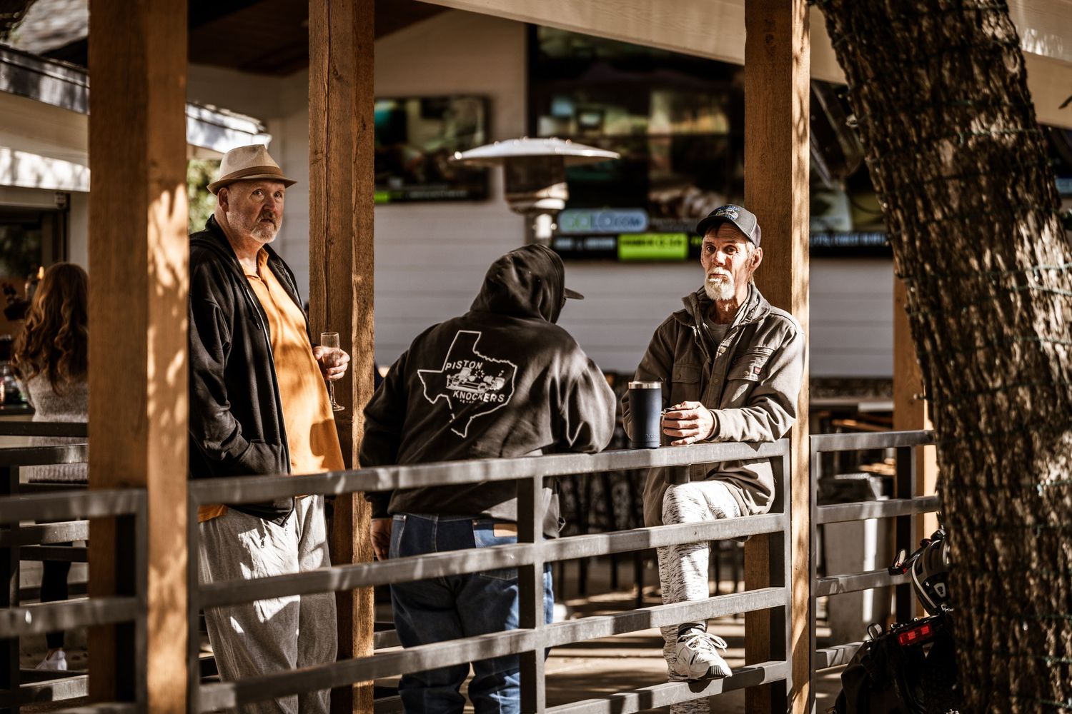 Car enthusiasts gathered on a covered wooden deck at an automotive event.