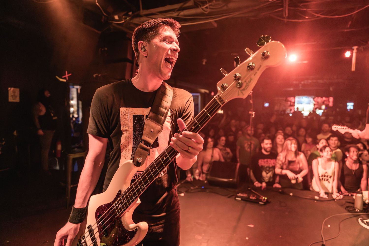 Bass player performs with intensity under red stage lighting at a live concert.