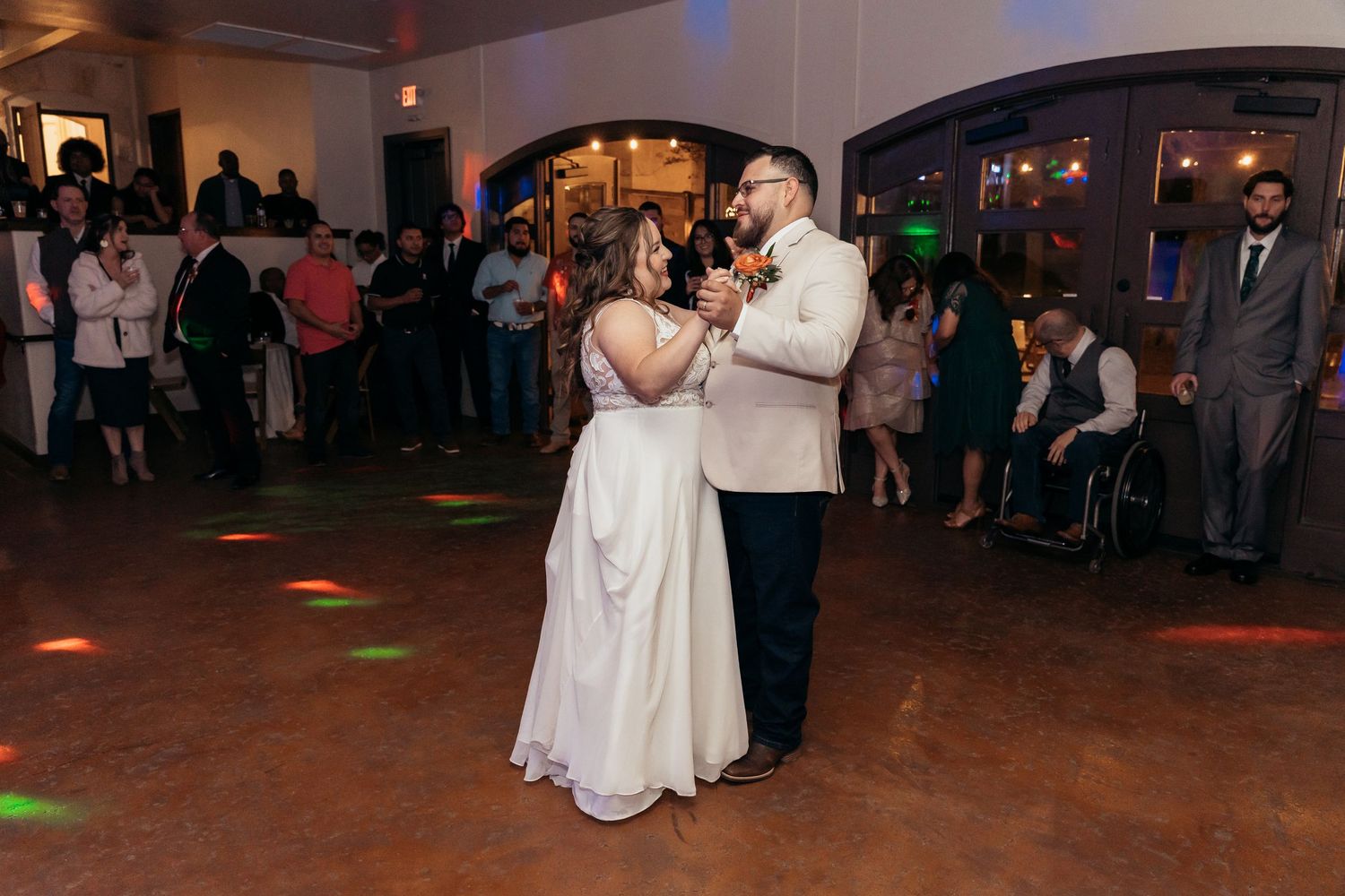 Couple shares a romantic slow dance at their wedding reception with colorful lights in the background.
