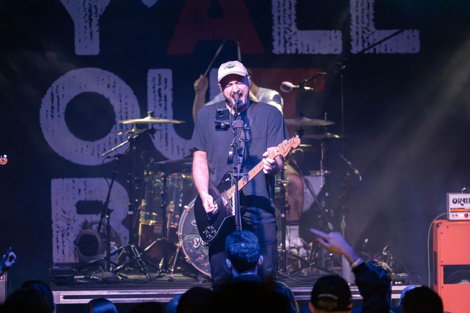 Musician performs with guitar on stage under bright concert lighting.