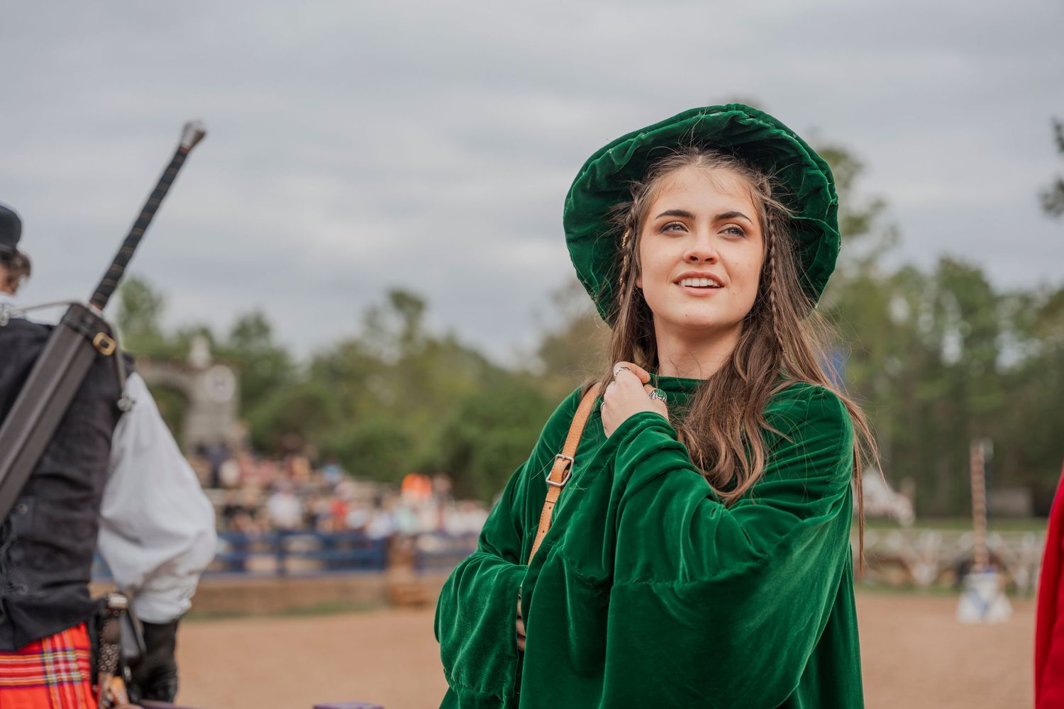 Person in emerald green velvet renaissance costume with matching hat at outdoor festival.