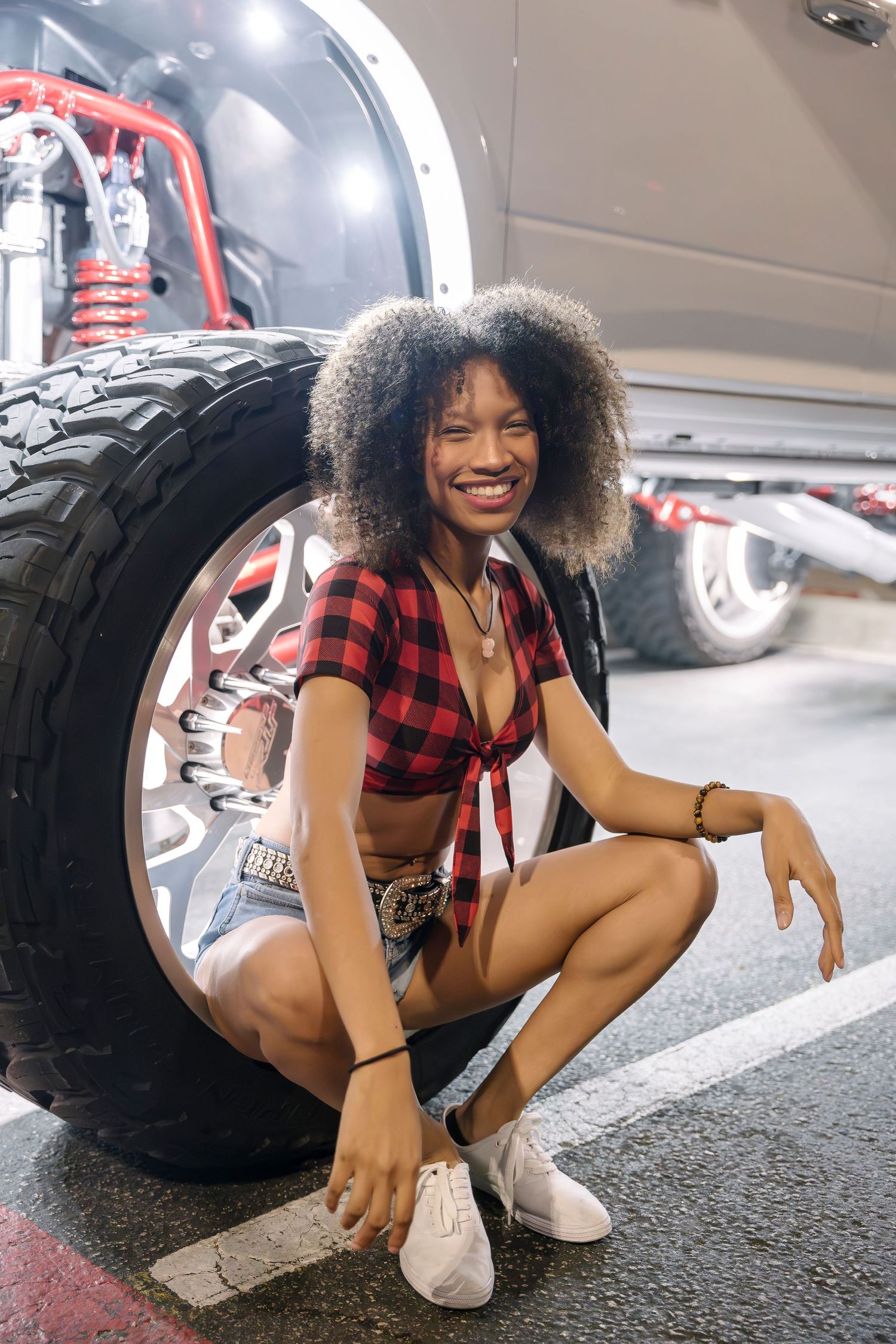 Buffalo plaid crop top styled with denim beside large off-road tire.