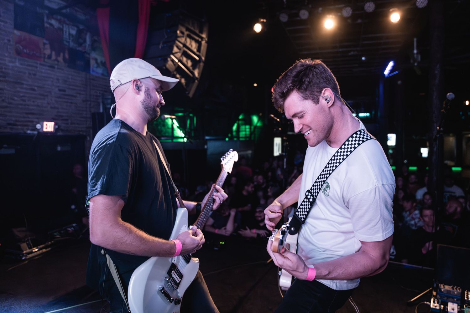 Two guitarists performing together on stage under concert lighting.