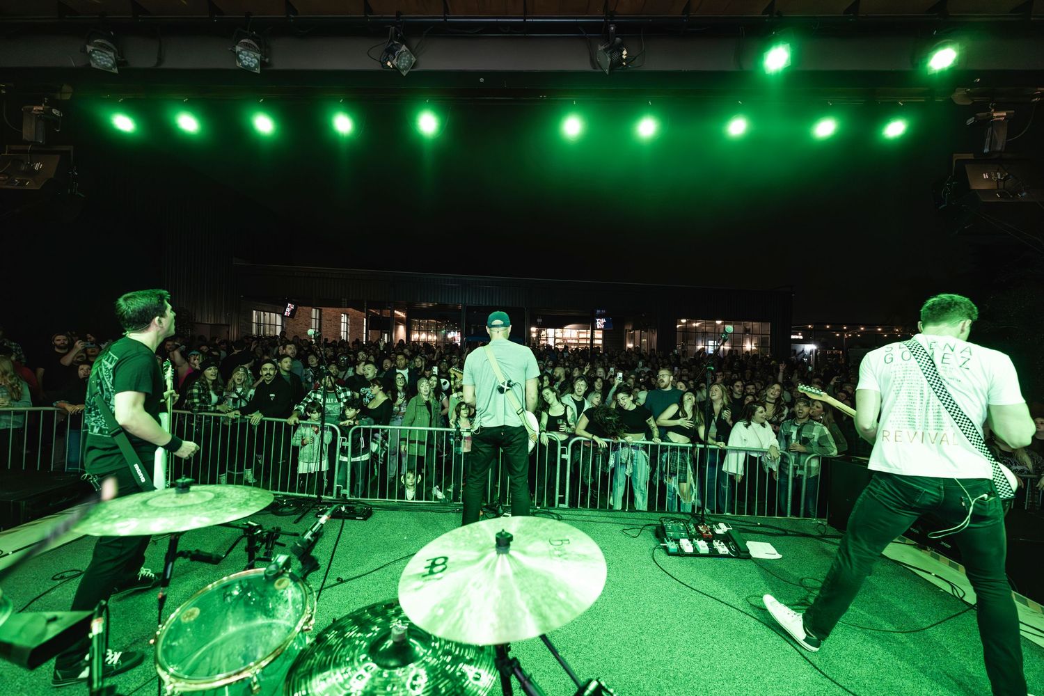 Band performing on stage with green lighting and crowd visible in foreground.