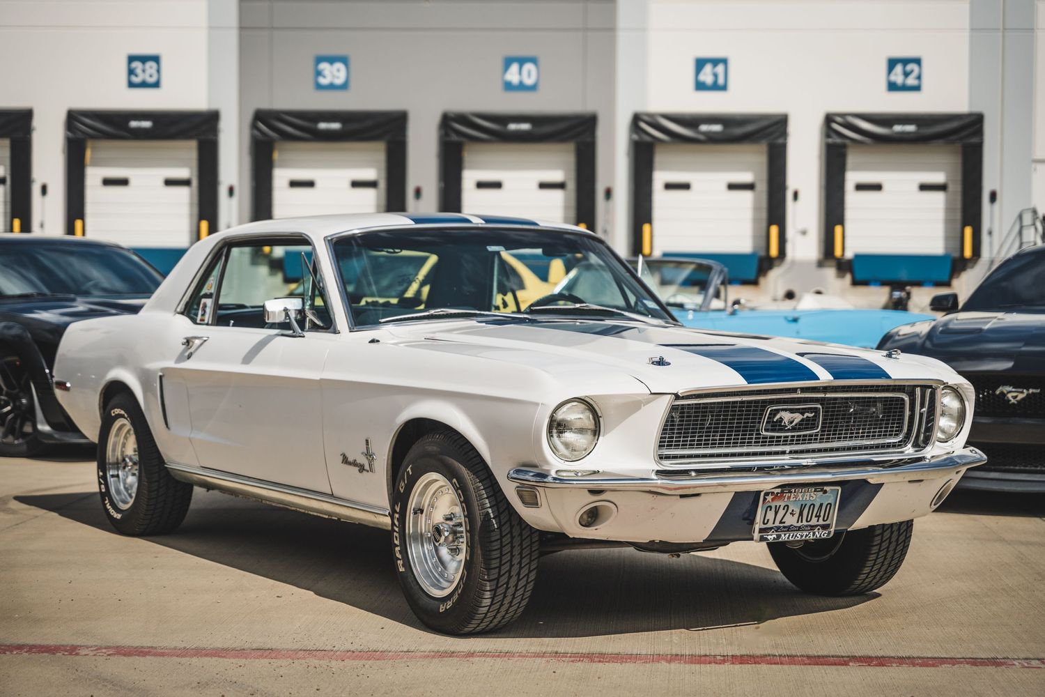 Classic white 1968 Ford Mustang coupe with vintage styling parked at industrial loading dock.