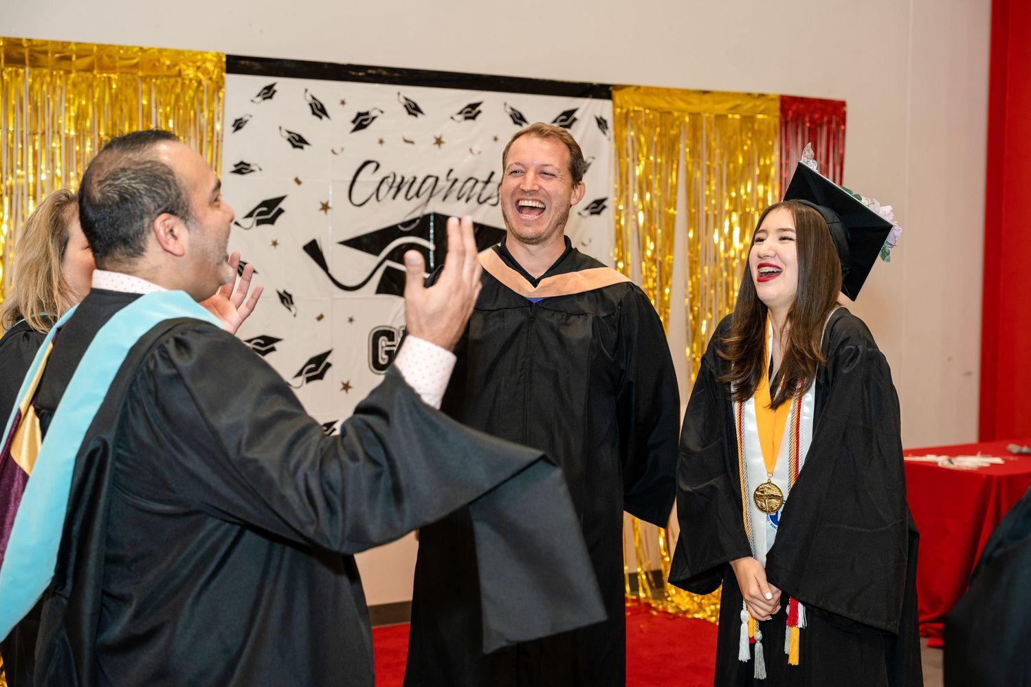 Graduation celebration moment against gold backdrop with mortarboard pattern.