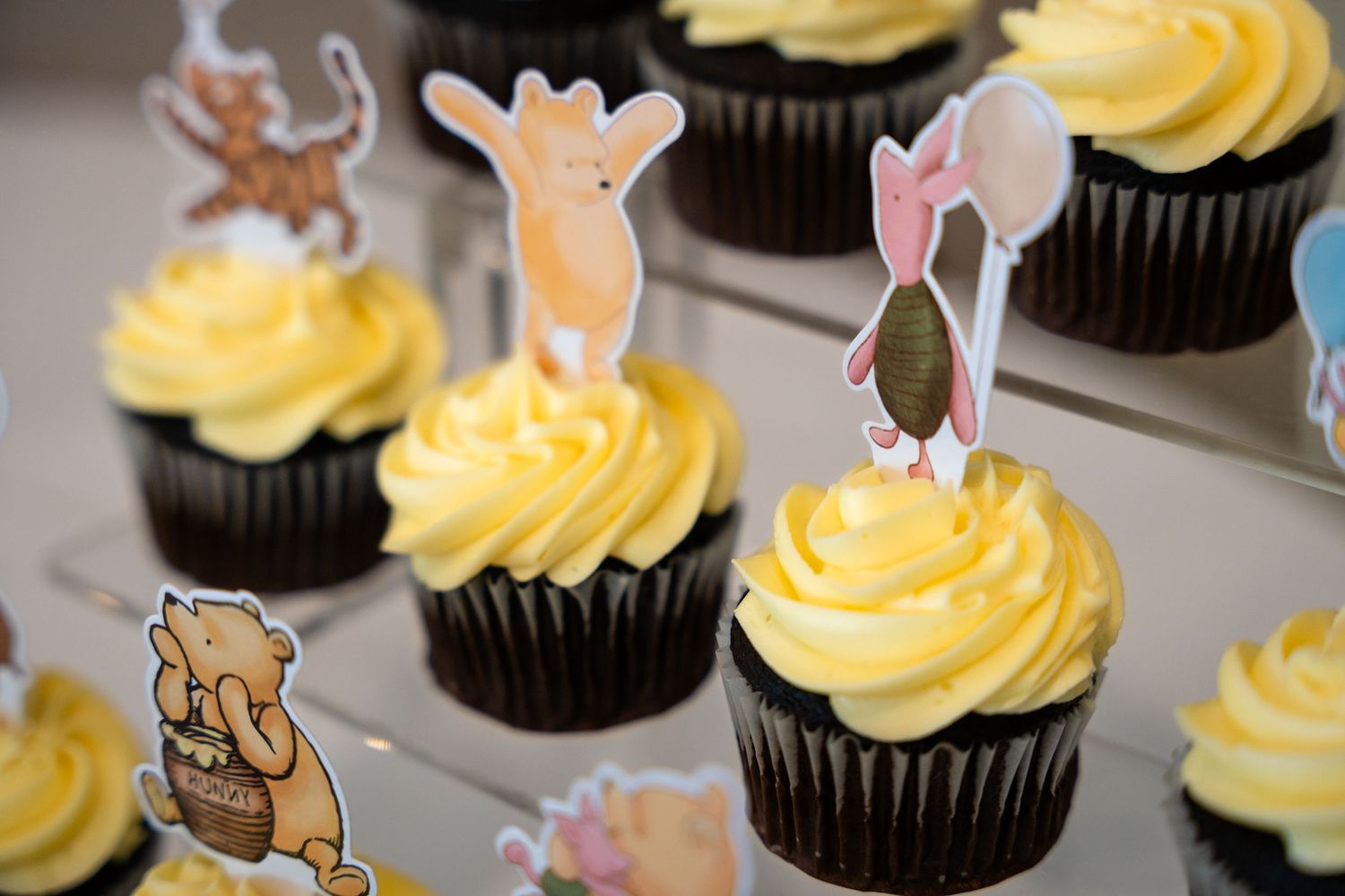 Chocolate cupcakes with yellow frosting topped with Winnie the Pooh character decorations.