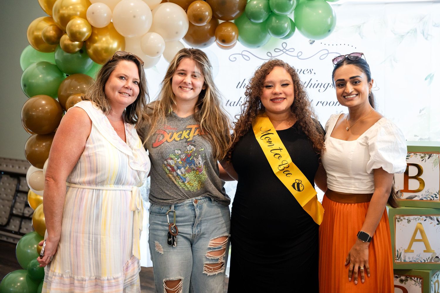 A celebratory event with guests posing under a festive balloon arch in gold, white and green colors.