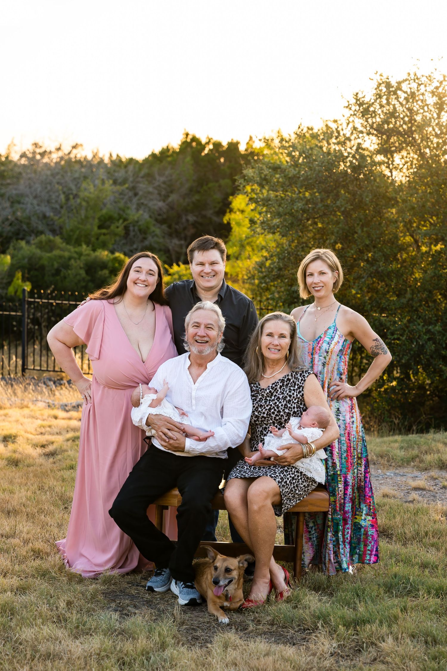 Family portrait with twins, dog, and multi-generational group in scenic outdoor setting at sunset.