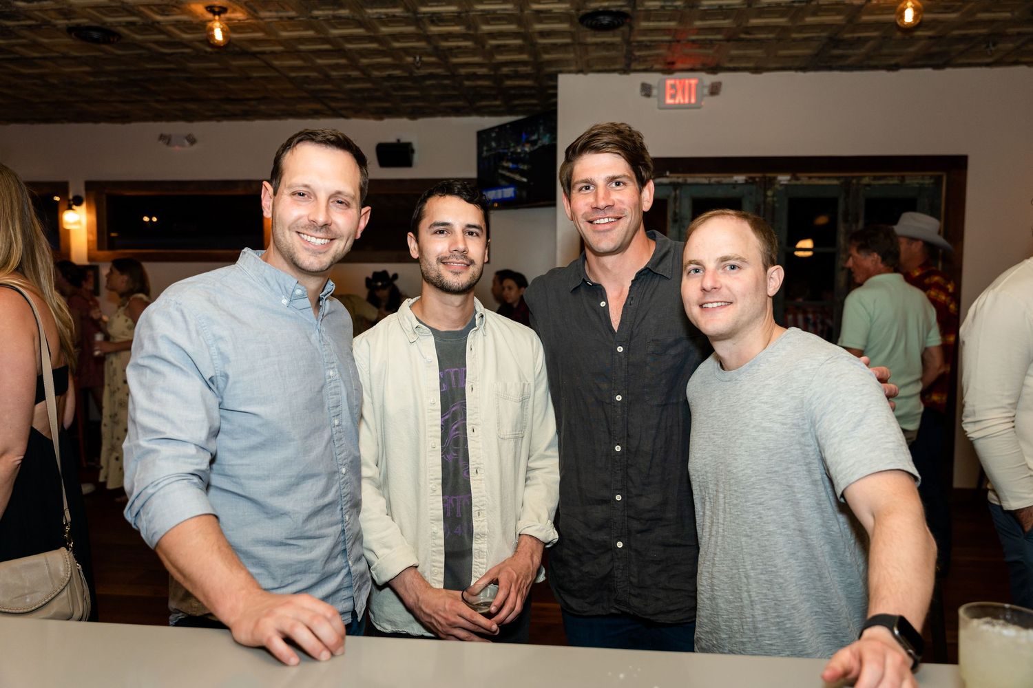 Four friends gather for drinks at a restaurant bar under warm evening lighting.