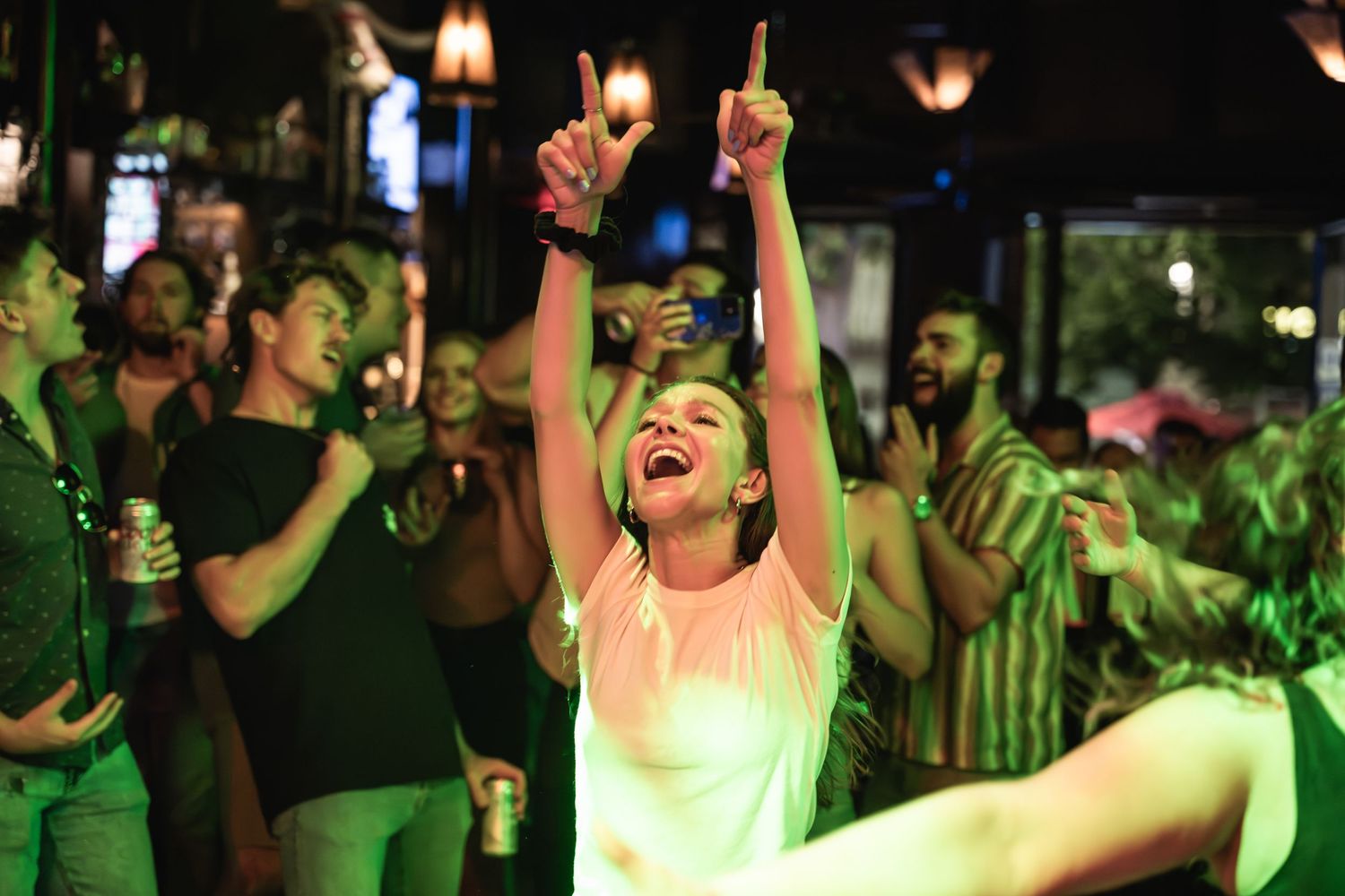 Concert goer raises arms joyfully during music performance under stage lights.