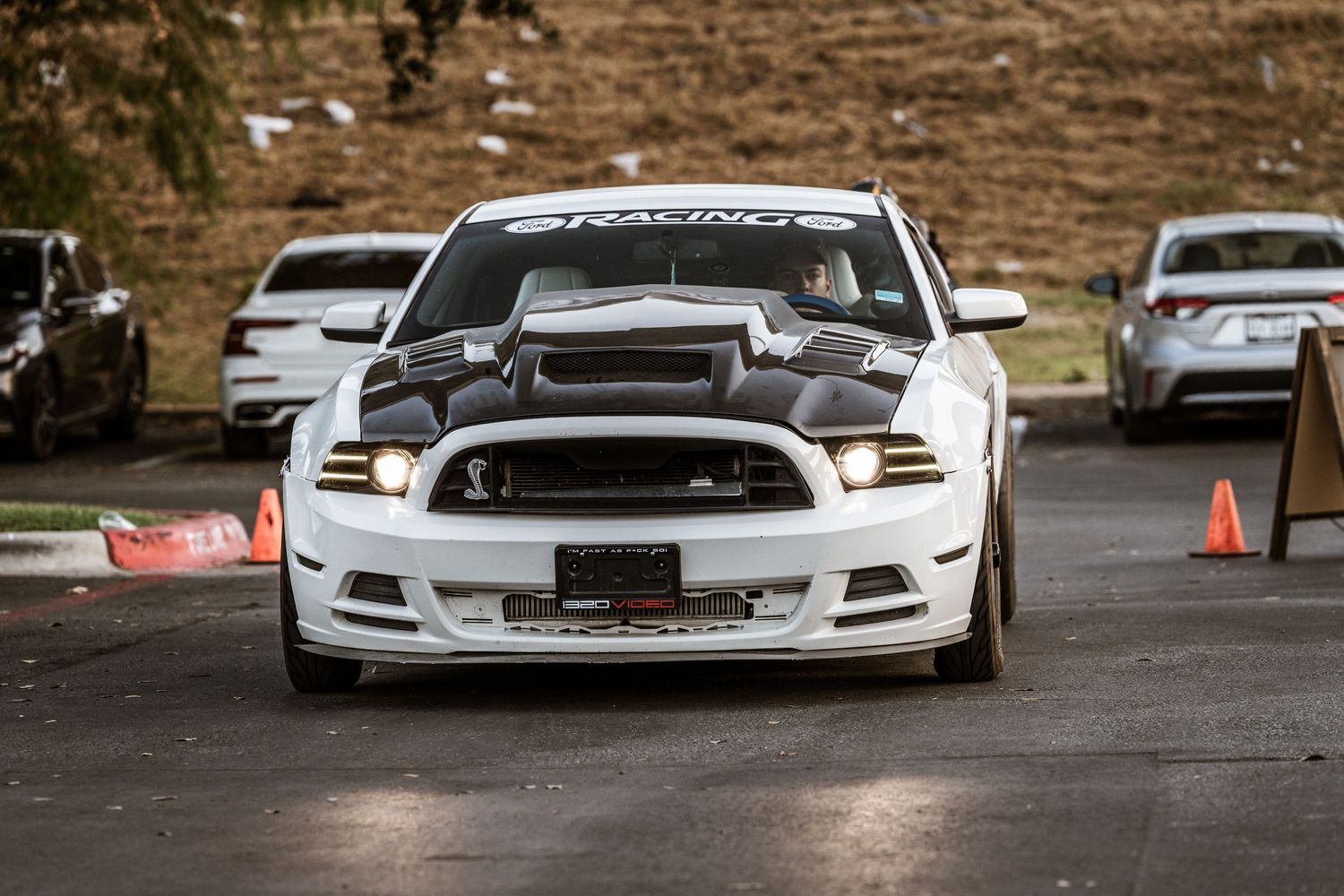Modified white Ford Mustang with custom hood and body kit parked in a lot.