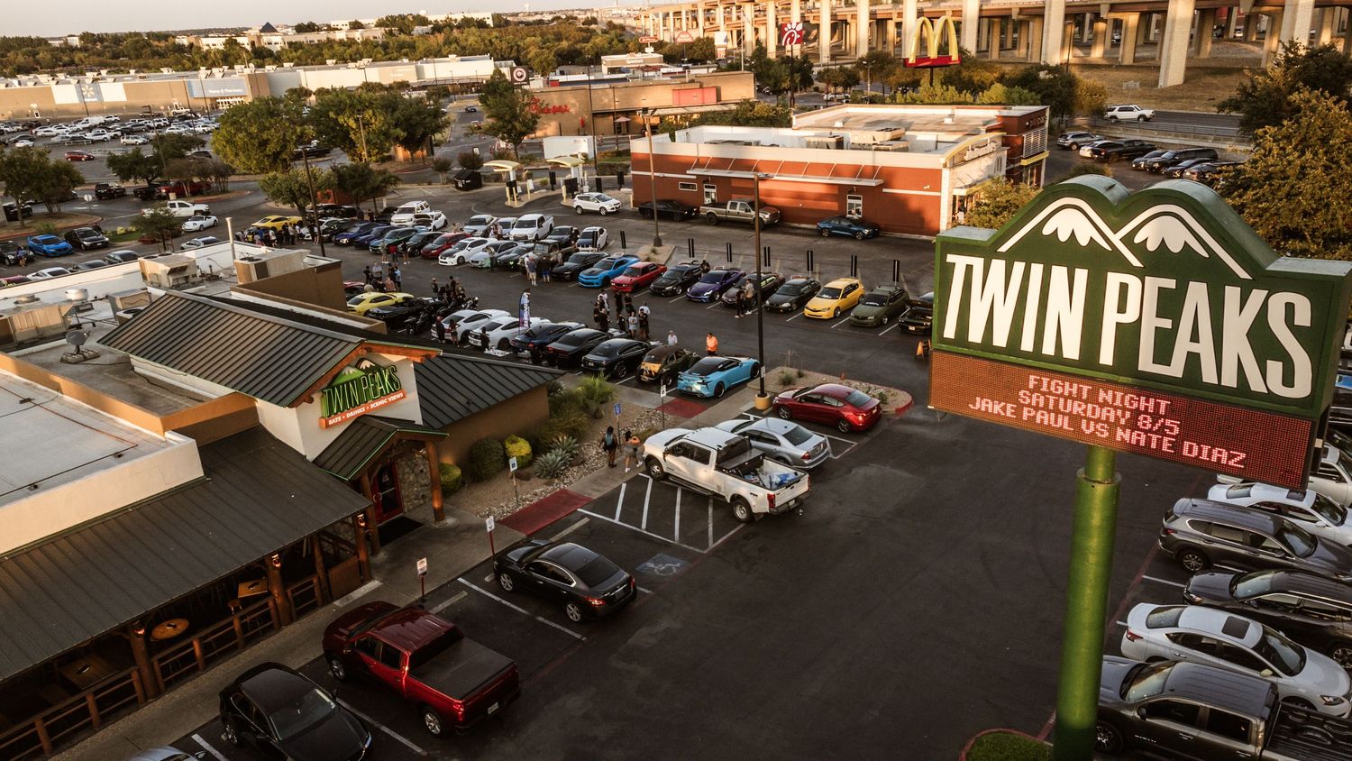 Aerial shot of Twin Peaks parking lot during sunset filled with cars at an auto gathering.