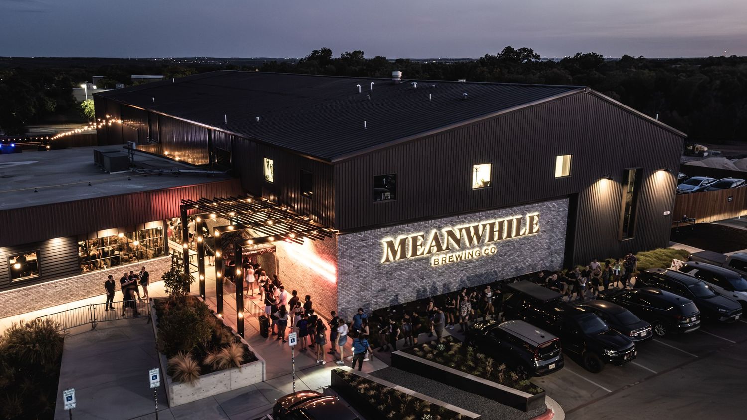 An aerial view of a lit-up venue called Meanswitch at night with cars parked outside.