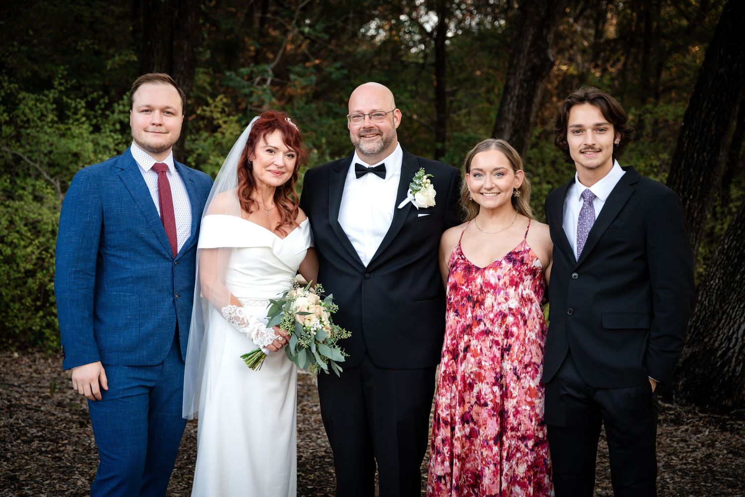 Family formal portrait outdoors with wedding couple and guests in formal attire.