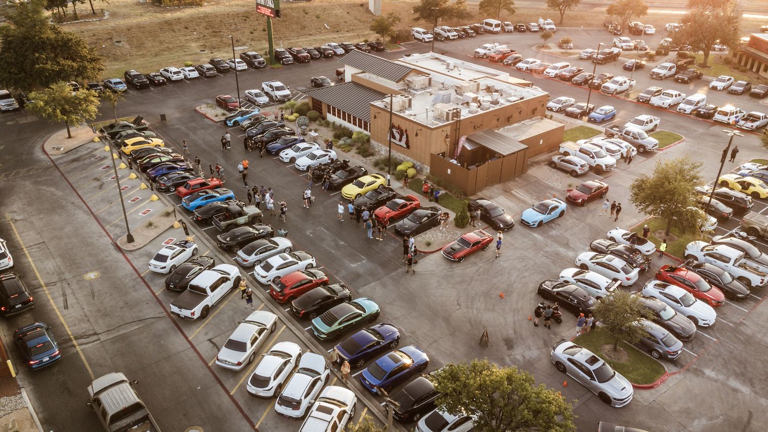 Aerial view of a crowded car show parking lot filled with various vehicles.