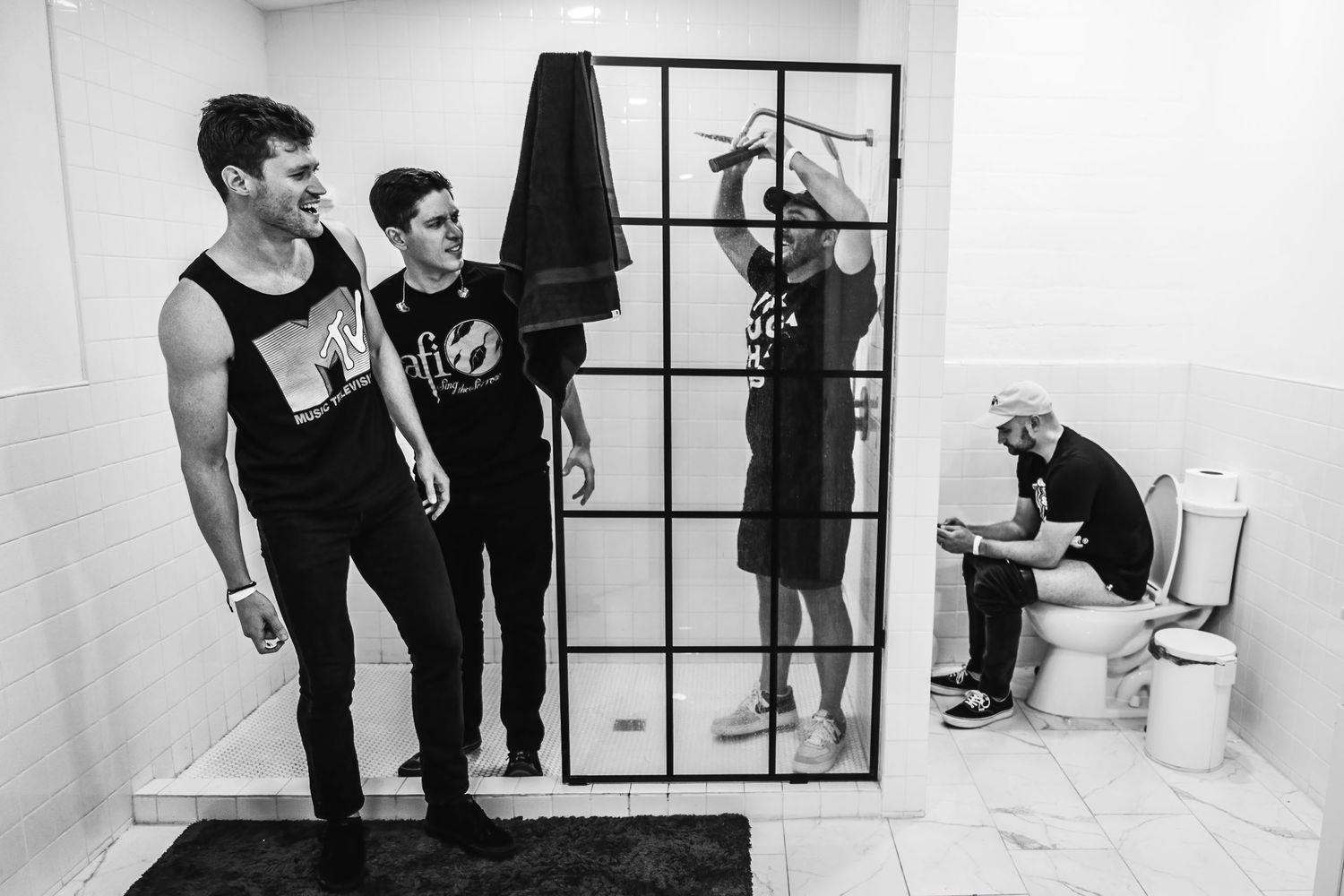 Musicians pose humorously in a bathroom with one member seated on a toilet.