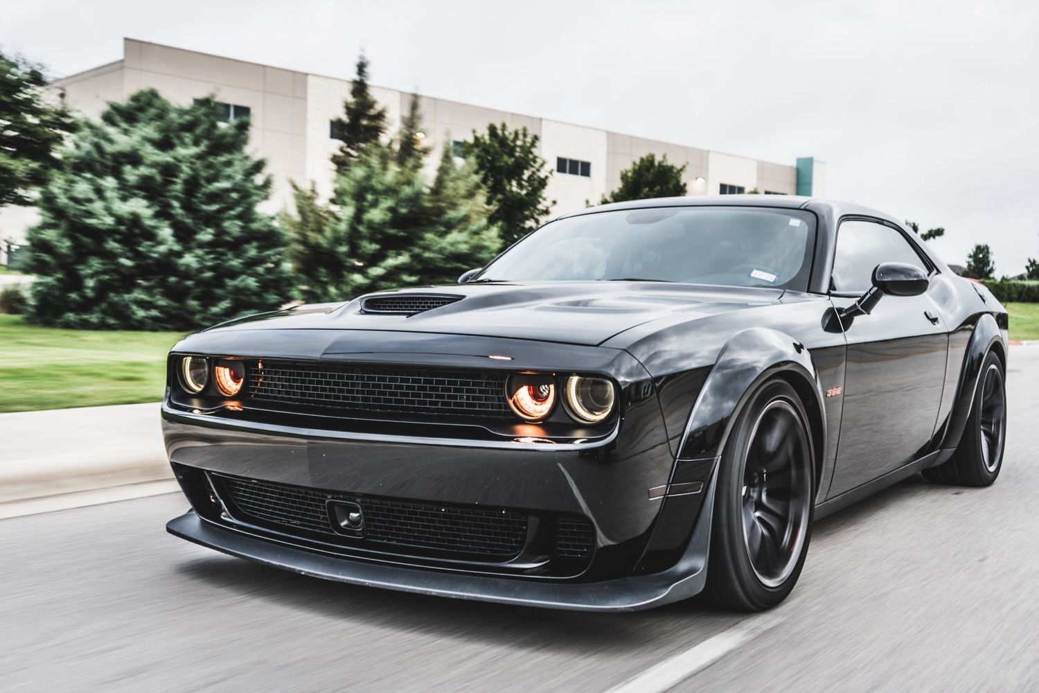Black Dodge Challenger with aggressive body kit and wide wheels driving on city street.